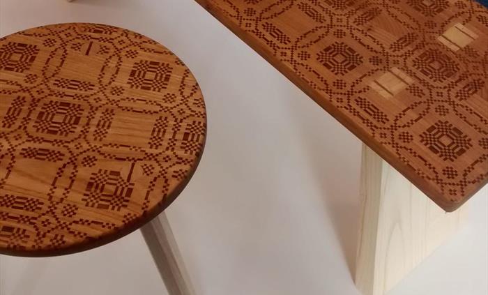 Aerial view of highly patterned round wooden stool next to a long rectangular bench also in wood. Both have geometric etched patterns and detailing of